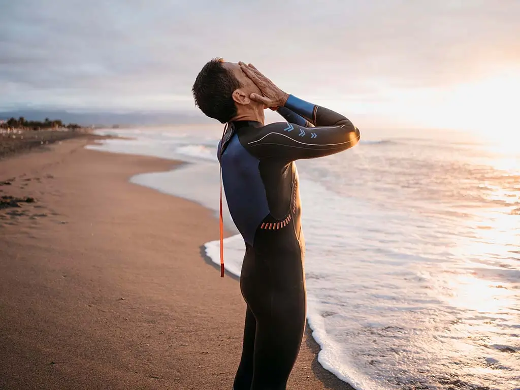 Exhausted man sitting on the beach after surfing with his hands covering his face